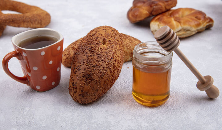 肉侧视图美味芝麻饼与一杯茶和蜂蜜在一个玻璃罐上的白色背景蜂蜜壁板杯子
