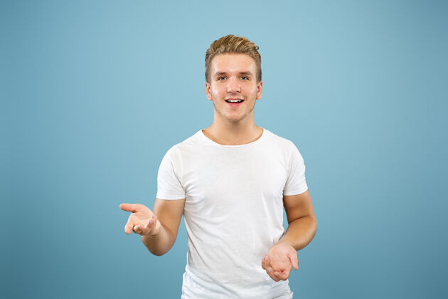事业蓝色工作室背景上的白人年轻人半身肖像穿着衬衫的漂亮男模人类情感的概念 面部表情 销售 广告指向和展示某物成人男性人