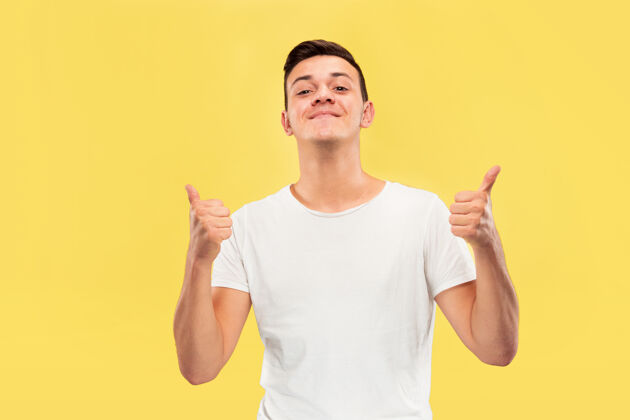 年轻黄色工作室背景上的白人年轻人半身肖像穿着衬衫的漂亮男模人类情感的概念 面部表情 销售 广告竖起大拇指 快乐成人成功肖像