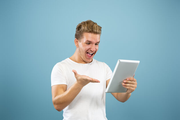 员工在蓝色工作室背景上的白人年轻人半身肖像穿着衬衫的漂亮男模人类情感的概念 面部表情 销售 广告使用平板电脑进行虚拟博客 自拍 学习成人公司面部
