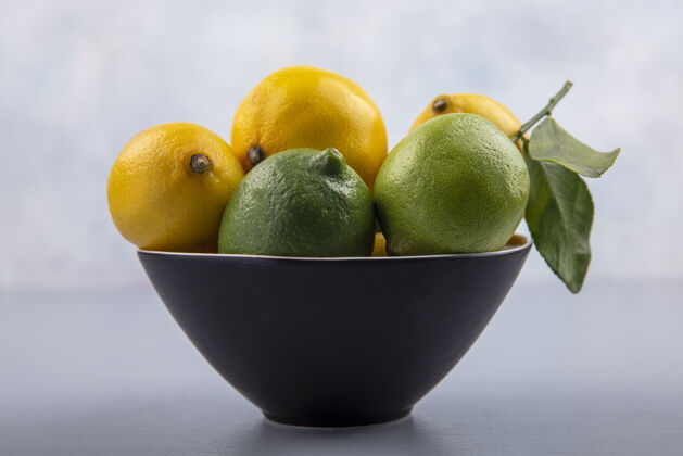 黑灰色背景上黑色碗中的柠檬和酸橙的前视图柑橘视野前面