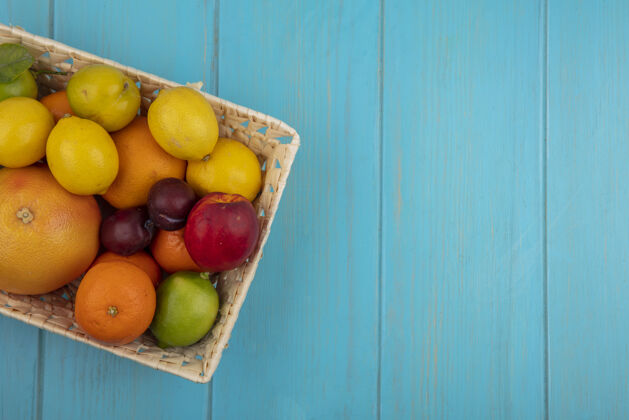 橘子顶视图复制空间水果混合葡萄柚柠檬柠檬橙子桃子和李子在一个蓝绿色的背景篮子混合绿松石复制