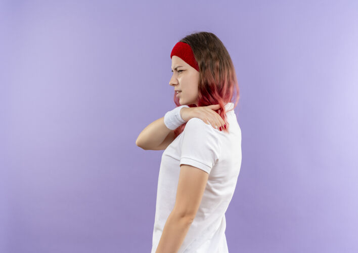 运动年轻的运动型女人摸她的肩膀感觉疼痛站在一边紫色的墙壁侧身女人人