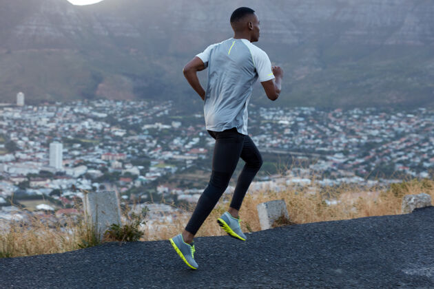 民族男性慢跑者的动作视图包括长距离 穿着休闲紧身裤和t恤 在公路上的山景上摆姿势 穿着运动鞋 在有氧运动中呼吸动作 速度概念跑步公路速度