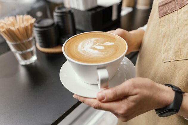咖啡师女咖啡师手拿装饰好的咖啡杯的侧视图女服务员专业