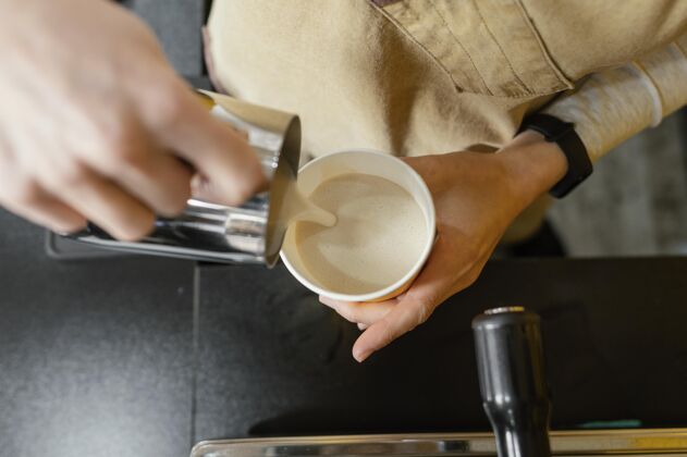 雇员女咖啡师往杯子里倒泡沫牛奶的俯视图女女职业