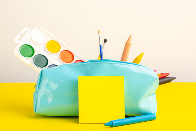 钢笔黄色书桌上蓝色笔盒内的不同颜色的铅笔和颜料记事本学校油漆