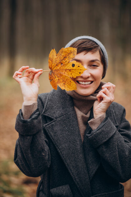 时尚秋天公园里的年轻女子 捧着树叶的脸衣服贝雷帽模特