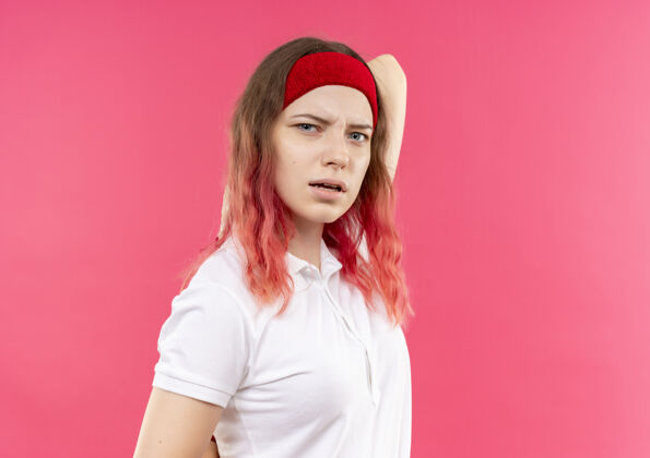 看戴着头巾的年轻运动女郎站在粉红色的墙上 困惑而不确定运动公动装