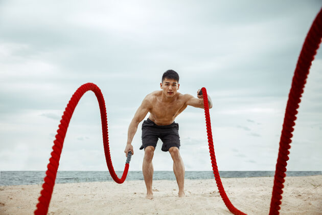 健美年轻健康的男子运动员在海滩上做深蹲男孩赤膊肌肉