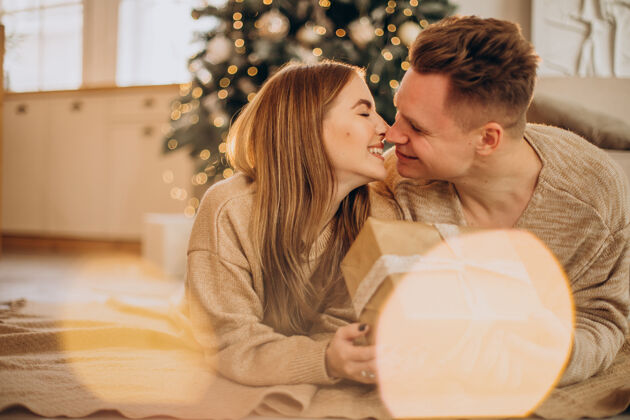 男人一对年轻夫妇在圣诞树旁互相制作礼物女朋友庆祝有趣