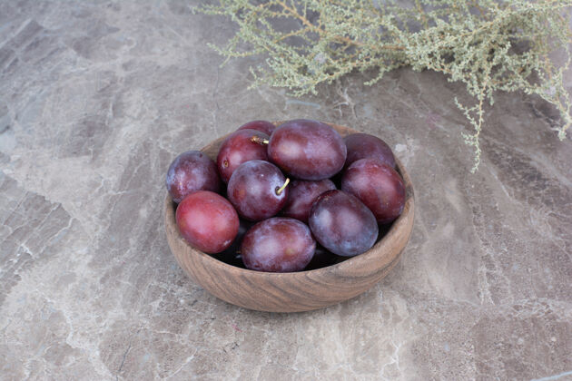 紫色在石头背景上的木碗里放上新鲜的李子天然水果美味