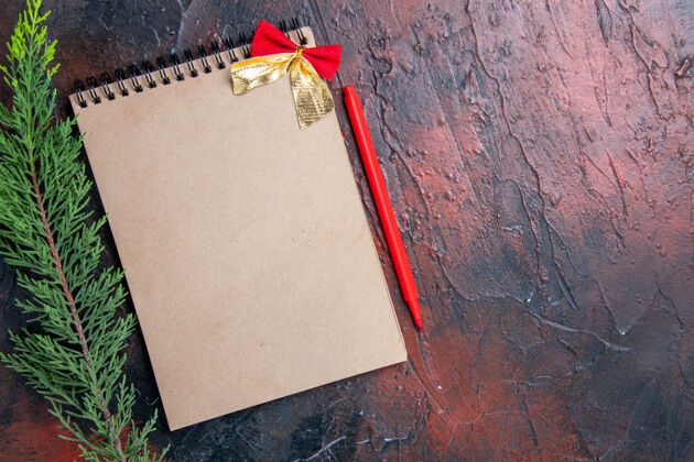 钢笔顶视图红笔一个小蝴蝶结的记事本一根松枝在暗红色的表面复制空间笔记本笔记空白