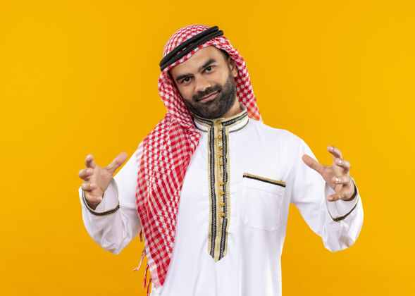 站立身着传统服装的阿拉伯商人展现出大号手势 双手自信地微笑着 测量符号站在橙色的墙上尺寸测量传统