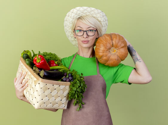 头发一个年轻的园丁 围着围裙 戴着帽子 手里拿着南瓜自信抱蔬菜