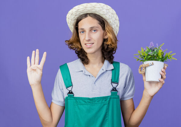 站着年轻的园丁 穿着连体衣 戴着帽子 微笑着捧着盆栽植物四数字帽子