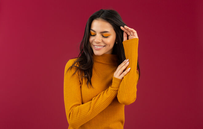 成人美丽的微笑 时尚的深色皮肤 穿着黄色秋冬时装毛衣的西班牙女人的画像 在红墙上摆出孤立的姿势女士微笑女性