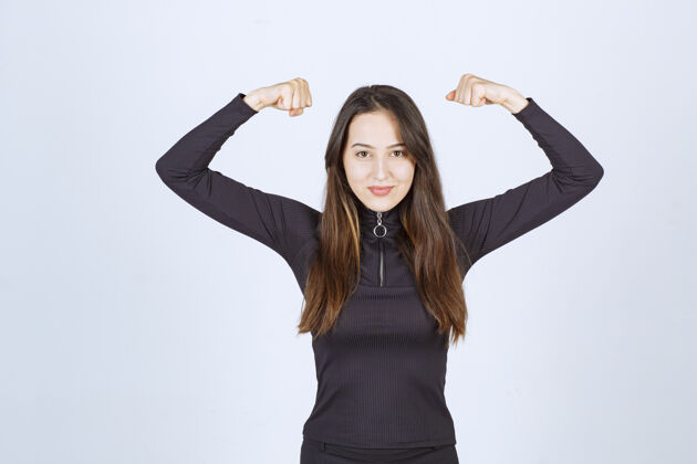 女人穿黑色衣服的女孩露出她的拳头和手臂肌肉人女人休闲