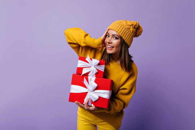 欧洲快乐的戴着黄色帽子的女孩在为圣诞节做准备快乐的高加索女士在紫色的房间里摆着新年礼物的肖像表情可爱礼物