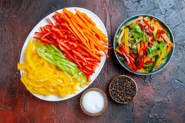 晚餐顶视图彩色切辣椒在白色盘子蔬菜沙拉在碗黑胡椒盐大蒜在深红色的桌子上顶部菜盘子