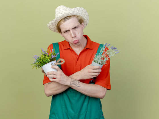 光年轻的园丁 穿着连体衣 戴着帽子 手里拿着盆栽植物立场连身衣举行