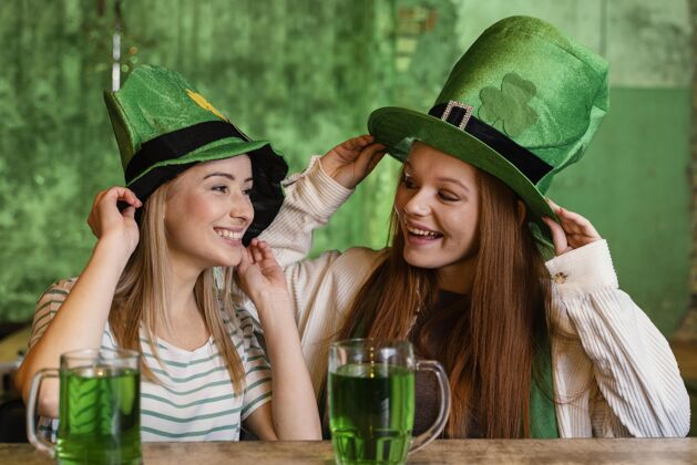 饮料快乐的女性朋友一起在酒吧庆祝圣帕特里克节幸运绿色帽子