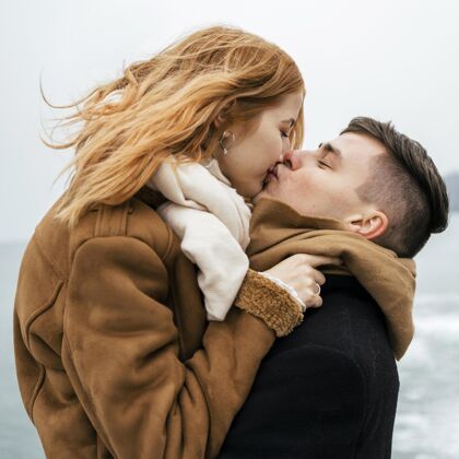 男人冬季接吻时湖边情侣的侧视图冒险户外女人
