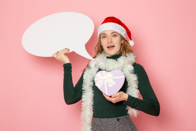 情感正面图年轻女性手持白色大招牌 呈现在粉色墙上的模特圣诞新年假期色彩感慨圣诞风景漂亮