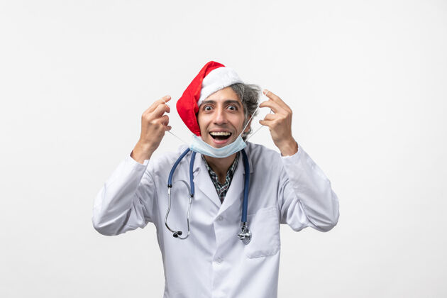 冠状病毒正面图：男医生拿着口罩在白色墙壁上 感染了新年假期病毒药品圣诞节视图