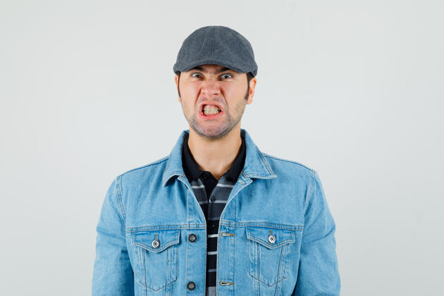 男性戴帽子 穿t恤 穿夹克的年轻人咬牙切齿 看上去很生气发型牙齿现代