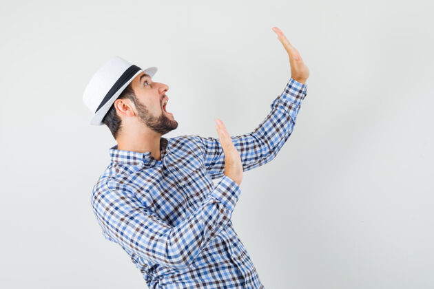 帽子年轻男性穿着格子衬衫 戴着帽子 以预防性的方式保持双手 看上去很害怕正面图前面肖像成功