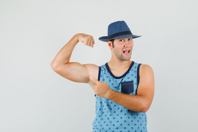 自信穿蓝色单品的年轻人 帽子指着胳膊上的肌肉 看上去很强壮强壮胡须男人