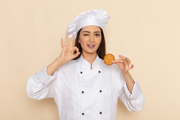 烹饪身穿白色厨师服的年轻女厨师正拿着饼干站在浅白的墙上快乐年轻人