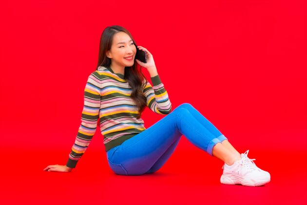手机肖像美丽的亚洲年轻女子在红色隔离墙上使用智能手机女性购买聪明