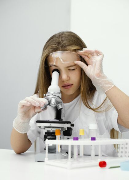 显微镜年轻有趣的女科学家用显微镜教育实验室外套实验