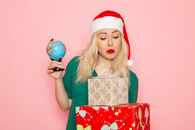 地球正面图年轻女性手持地球仪和圣诞礼物在粉红色墙上的照片模特妇女圣诞节新年的颜色风景年轻的女性颜色