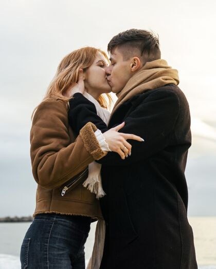 探索冬天在海边接吻的年轻夫妇的侧视图海滩男人冬天