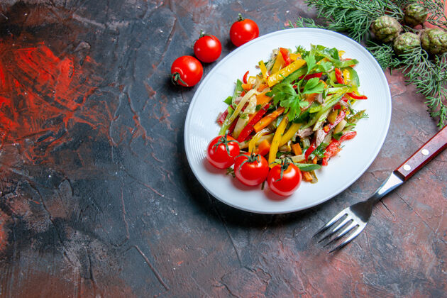 午餐俯视图蔬菜沙拉在椭圆形盘子叉樱桃西红柿在深红色的桌子上餐胡椒叉子