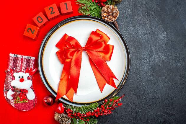 餐盘礼品俯视图 餐盘上有彩带装饰配件杉木树枝和数字圣诞袜 红色餐巾上有黑色背景袜子餐巾圣诞节