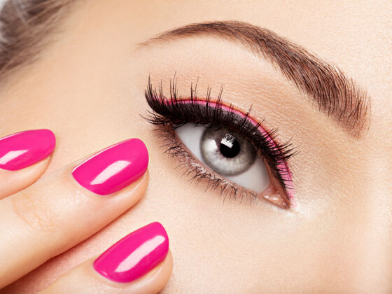 魅力特写镜头：眼睛附近有粉色指甲的女人的脸粉色指甲的指甲眼影高加索光泽