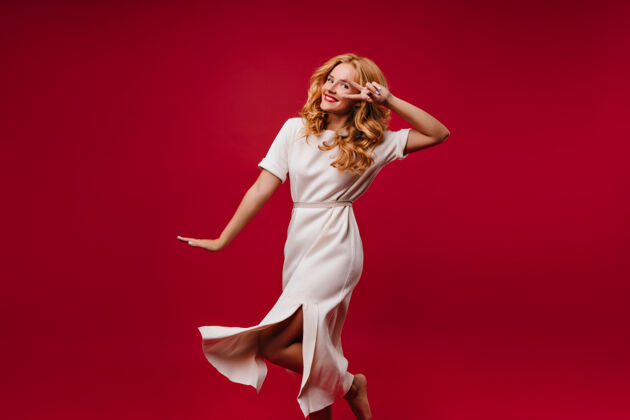 时尚美丽的白衣女人在表达幸福可爱的金发女孩在红墙上跳舞金发微笑成人