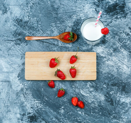 部分俯视图草莓与牛奶和一个深蓝色大理石表面上的木勺砧板水平块草莓草莓