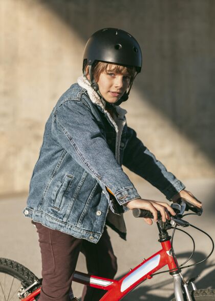 孩子戴着安全帽的男孩在自行车上摆姿势的侧视图自行车青年放松