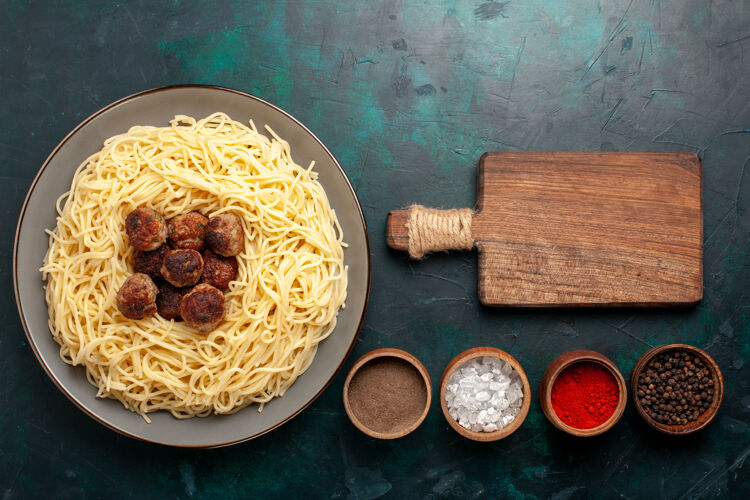 肉丸在深蓝色的桌子上俯瞰煮熟的意大利面食和肉丸和调味品配料餐面食