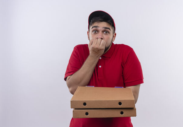 男人年轻的送货员穿着红色制服 戴着帽子 手里拿着一叠比萨饼盒 吓得咬指甲害怕红色盒子