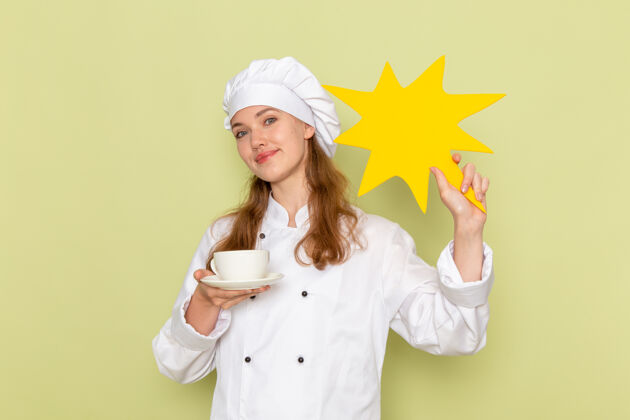 穿着女厨师身穿白色厨师服 手持黄色标志和绿色墙上的杯子手持人护士