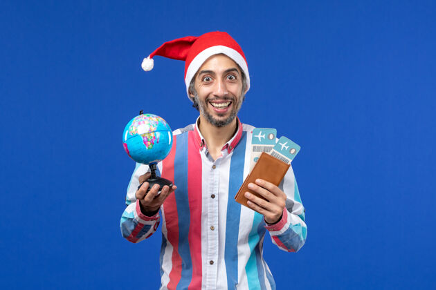 颜色前视图普通男性 带门票和地球仪 蓝色墙壁 节日新年色彩成人圣诞节喜剧演员