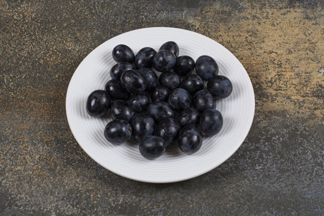 自然白盘子里放着新鲜的黑葡萄食品农业葡萄