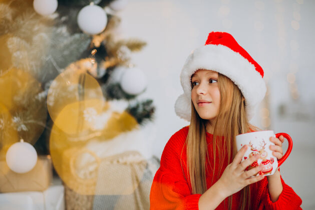 年轻在圣诞树旁喝可可的女孩礼物平安夜饮用
