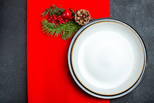 视图上图是黑色背景下 红色餐巾上装饰有针叶树圆锥体的空盘子和冷杉树枝配件瓷器圣诞节